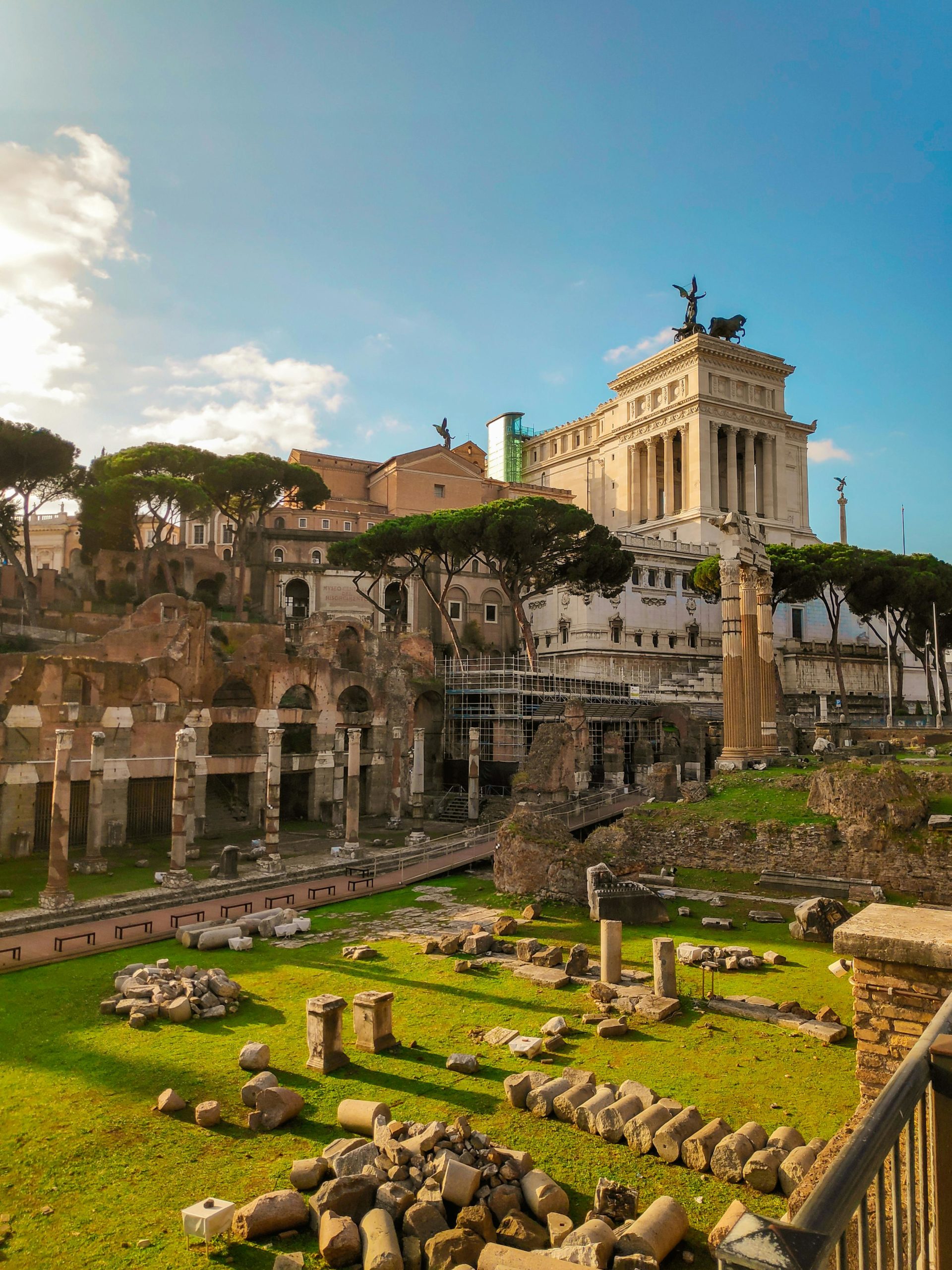 Ancient ruins of the Roman Forum with the Vittoriano monument rising above the historic landscape.